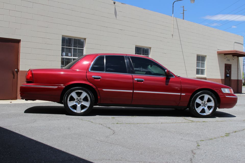 Red Mercury Grand Marquis sedan, passenger side profile, parked outside industrial building