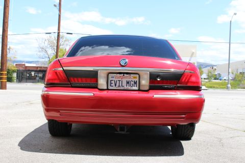 2003 Ford Crown Victoria - Straight-on rear view of a red Mercury sedan showing taillights, chrome bumper trim, and a California EVIL MGM license plate.