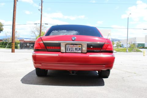 2003 Ford Crown Victoria - Red Mercury sedan photographed from directly behind, displaying its Mercury emblem and California EVIL MGM plate on an empty lot.