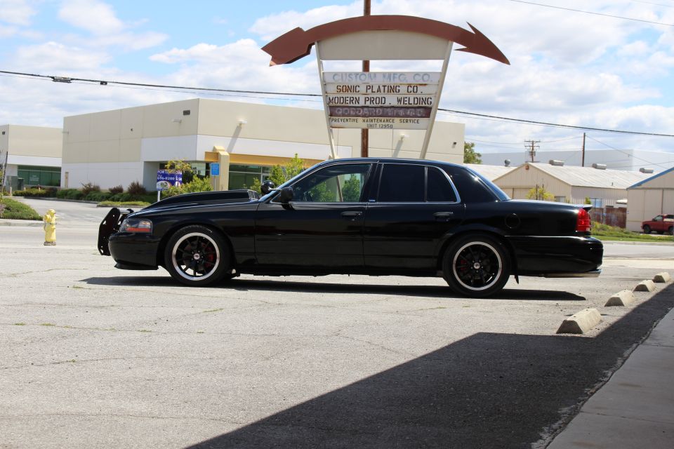 Black full-size sedan in profile parked under curved sign at industrial lot