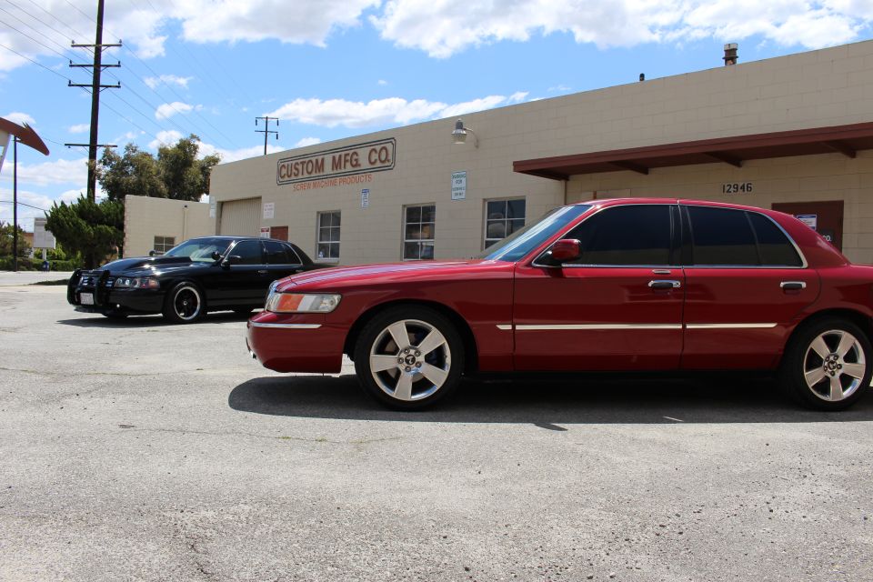 Red Mercury sedan front quarter with black sedan parked by Custom Mfg Co building
