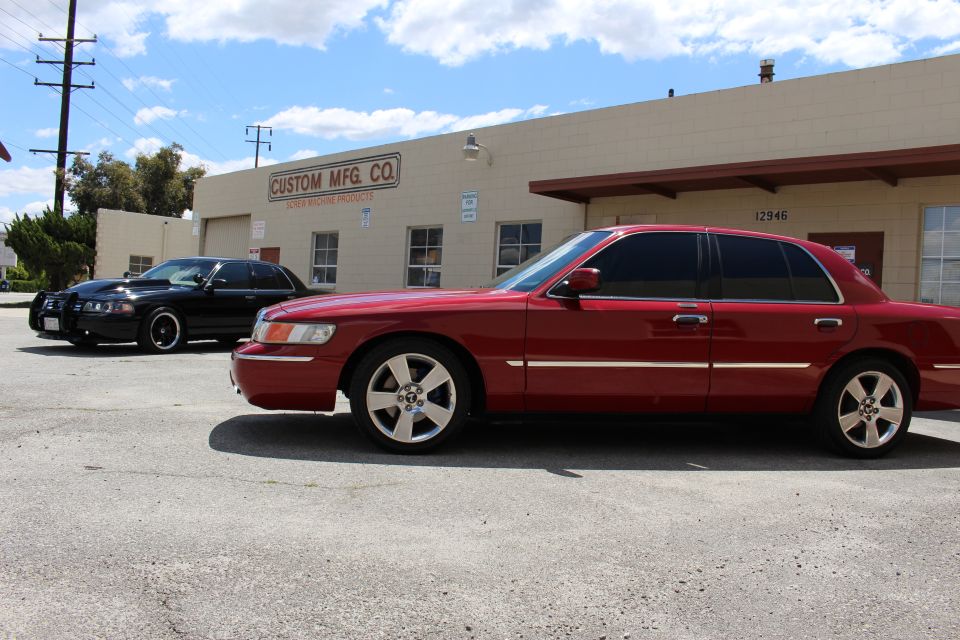 Red Mercury sedan side profile with black sedan near Custom Mfg Co building