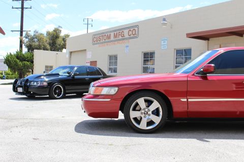 2003 Ford Crown Victoria - Tight front-quarter view of a red Mercury sedan's fender and machined wheel, with a black sedan parked nearby at Custom Mfg Co.