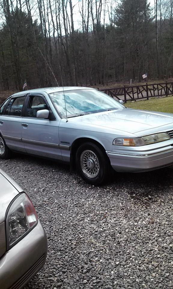 1994 Ford Crown Victoria parked on gravel, side view. Another car's front fender is visible on the left
