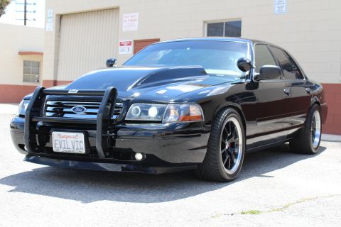 2003 Ford Crown Victoria - black Ford Crown Victoria with a chrome push bar and dark wheels, front three-quarter view, wearing a California EVIL VIC plate.