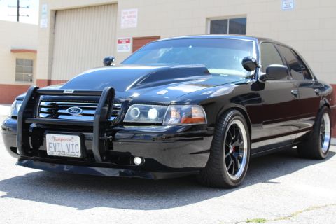 2003 Ford Crown Victoria - Black Ford Crown Victoria sedan with a brush guard and black wheels, front quarter view, displaying a California EVIL VIC license plate.