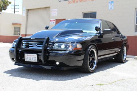 2003 Ford Crown Victoria - Lowered black Ford Crown Victoria with a chrome grille guard and EVIL VIC plate, parked outside an industrial building.