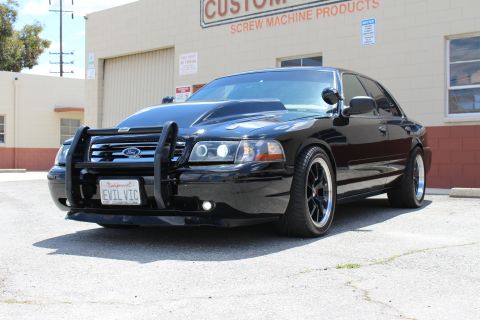 2003 Ford Crown Victoria - Black Ford Crown Victoria with a chrome grille guard and EVIL VIC plate, parked outside the Custom Mfg Co screw machine products building.