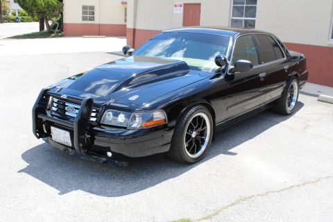 2003 Ford Crown Victoria - Black Ford Crown Victoria sedan with a black brush guard and dark wheels, shown in front three-quarter view at an industrial lot.