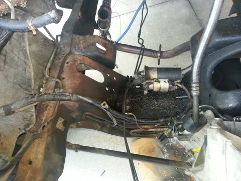 1994 Ford Bronco - Close-up view of engine bay components, including a starter motor and exhaust pipe, with visible rust and oil.