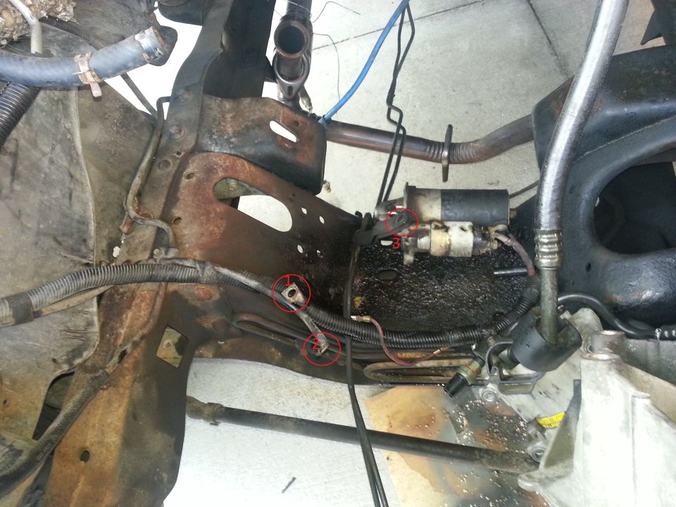 Starter motor mounted to rusty frame with hoses and wiring