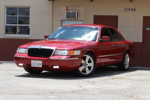2003 Ford Crown Victoria - red Mercury full-size sedan shown front three-quarter with chrome grille and EVIL MGM plate, parked by a building numbered 12946.