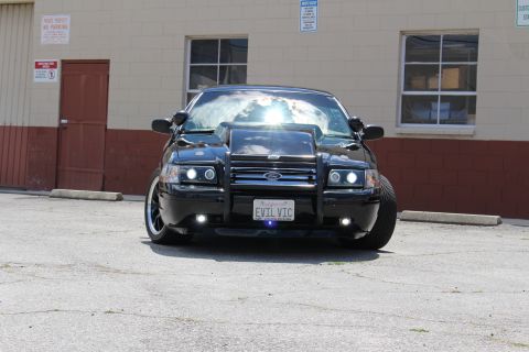 2003 Ford Crown Victoria - black Ford Crown Victoria shown head-on with chrome grille guard, fog lights and EVIL VIC plate, with bright sun glare on the windshield.