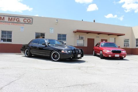 2003 Ford Crown Victoria - black Ford Crown Victoria and a red Mercury sedan parked in front of a building reading Custom MFG Co. Machine Products.