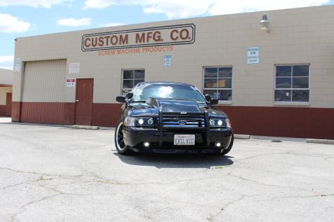 2003 Ford Crown Victoria - black Ford Crown Victoria with grille guard parked head-on before a building reading Custom MFG Co. Screw Machine Products.