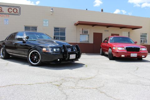 2003 Ford Crown Victoria - black Ford Crown Victoria with grille guard parked beside a red Mercury Grand Marquis outside a tan industrial building.