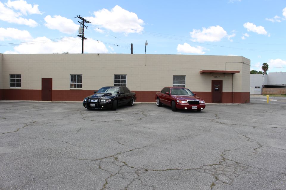 Distant black and red sedans parked by tan building under cloudy blue sky