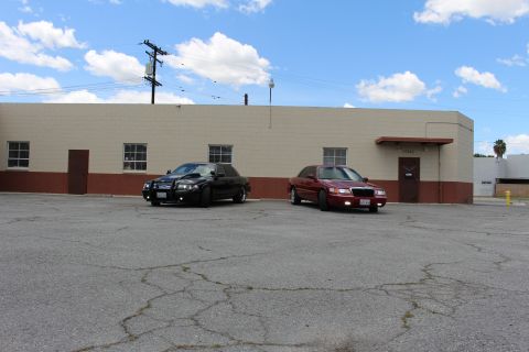 2003 Ford Crown Victoria - black Ford Crown Victoria and a dark red Mercury sedan parked by a tan industrial building under a partly cloudy sky.