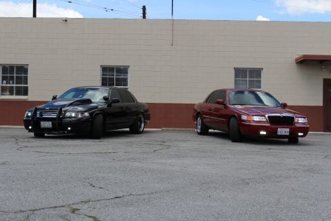 2003 Ford Crown Victoria - black Ford Crown Victoria with halo lights and grille guard parked next to a dark red Mercury Grand Marquis by a tan wall.