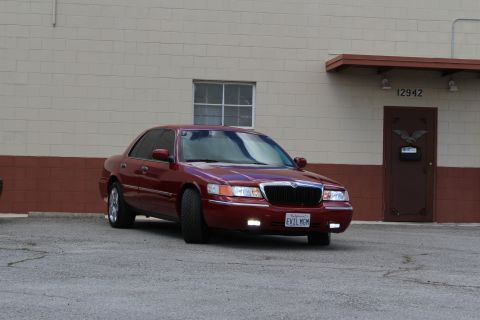 2003 Ford Crown Victoria - maroon Mercury Grand Marquis displays its chrome waterfall grille and California plate EVIL MOM in a parking lot.