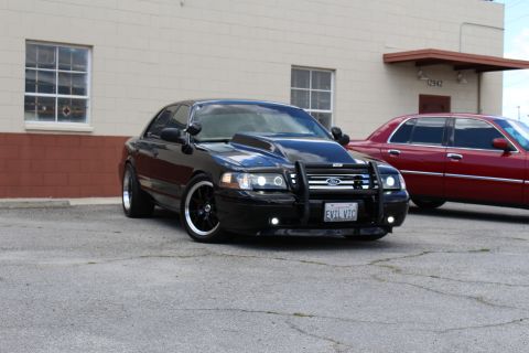 2003 Ford Crown Victoria - lowered black Ford Crown Victoria with push bumper and dark wheels sits angled, a maroon sedan visible at right.