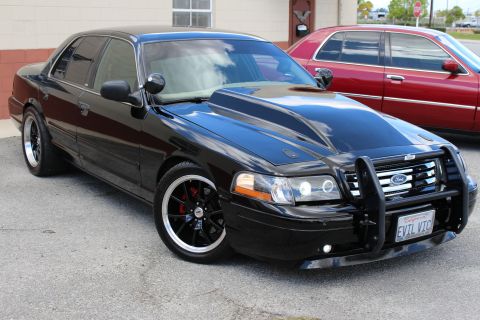 2003 Ford Crown Victoria - black Ford Crown Victoria with cowl-induction hood, push bumper and red brake calipers sits near a maroon sedan.