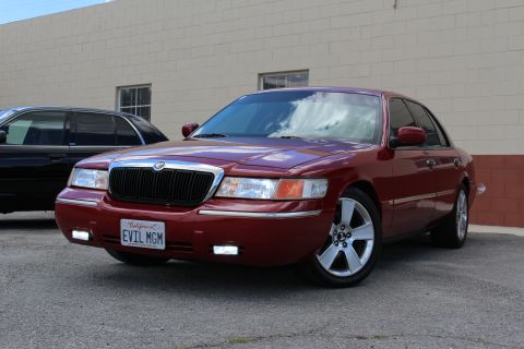 2003 Ford Crown Victoria - maroon Mercury Grand Marquis with chrome grille and plate EVIL MGM sits front-angled, a dark SUV partly visible at left.