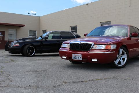 2003 Ford Crown Victoria - maroon Mercury Grand Marquis with plate EVIL MGM sits in front of a lowered black Ford sedan in a paved lot.