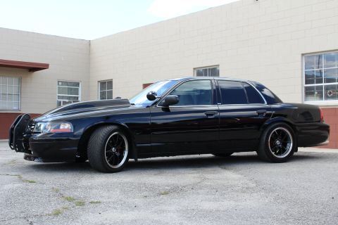 2003 Ford Crown Victoria - lowered black Ford Crown Victoria in side profile shows its push bumper, dark wheels and tinted windows.