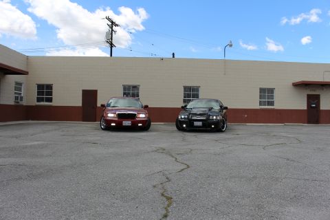 2003 Ford Crown Victoria - maroon Mercury sedan beside a black Ford sedan face the camera in a paved lot beneath a partly cloudy sky.