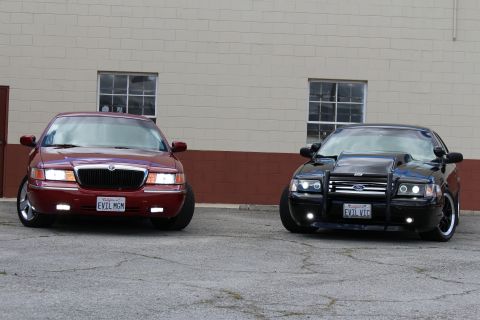 2003 Ford Crown Victoria - Front three-quarter view of a maroon Mercury sedan next to a lowered black Crown Victoria fitted with a grille guard.