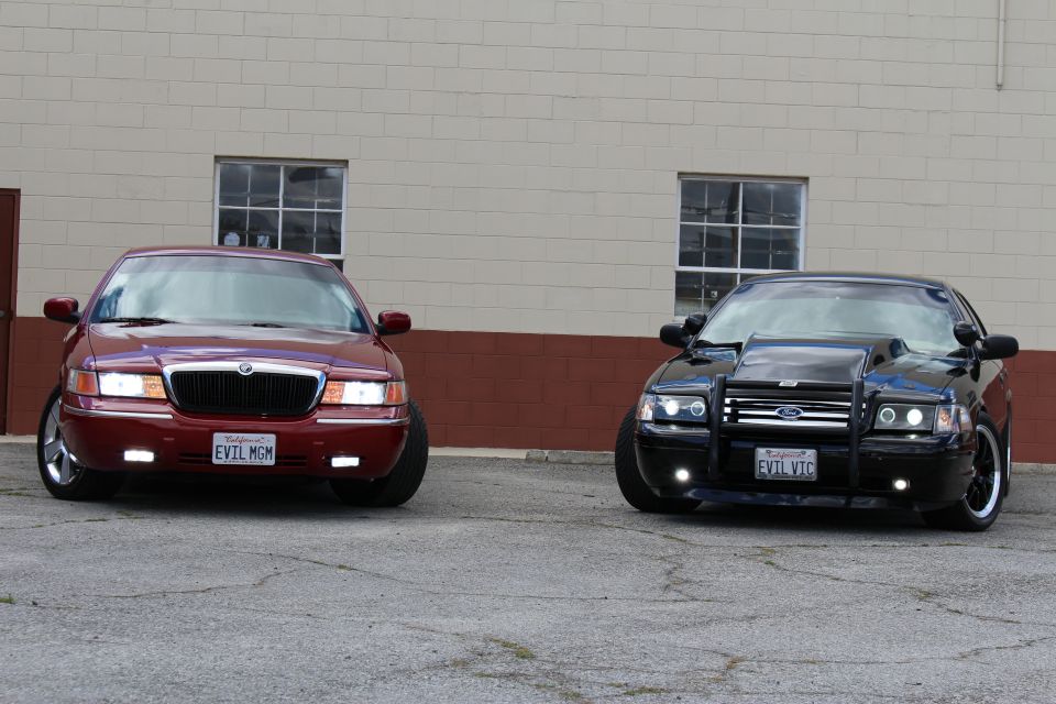 Maroon Mercury Grand Marquis beside black Crown Victoria with push bar, California plates