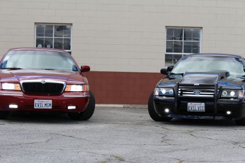 2003 Ford Crown Victoria - Tight front shot of a maroon Mercury Grand Marquis beside a black Crown Victoria wearing a push bar and white-letter plates.
