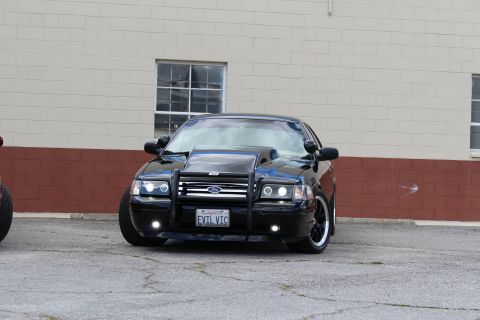 2003 Ford Crown Victoria - lowered black Ford Crown Victoria with a chrome grille guard and projector headlights sits before a tan industrial wall.