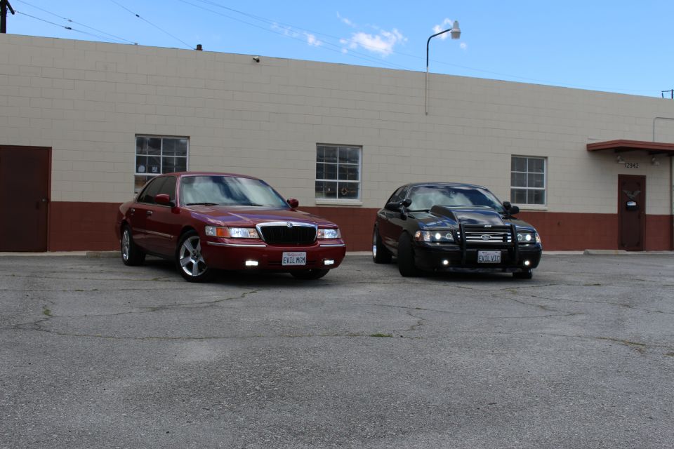 Maroon Mercury and black Crown Victoria with push bar parked side by side, blue sky