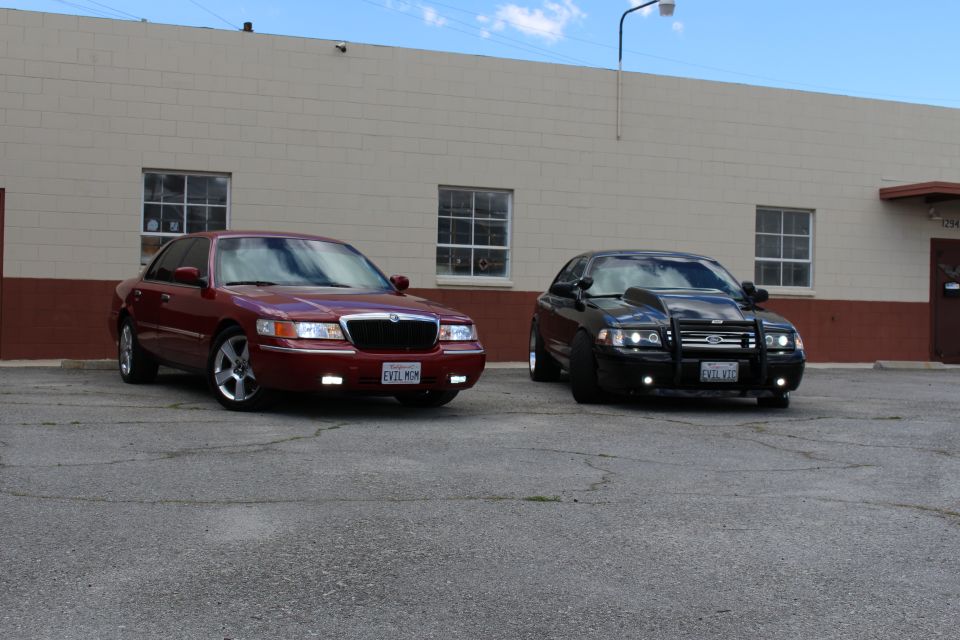 Maroon Mercury sedan and black Ford Crown Victoria with bull bar, front three-quarter
