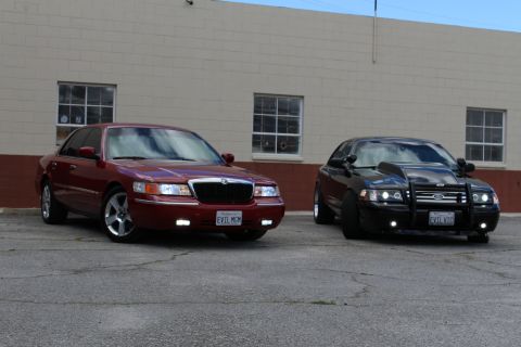 2003 Ford Crown Victoria - lowered maroon Mercury Grand Marquis sits next to a black Crown Victoria with a grille guard on cracked asphalt.