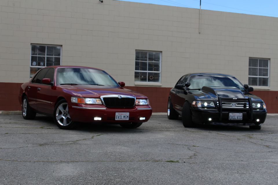 Maroon Mercury sedan and black Ford sedan with push bar parked under blue sky