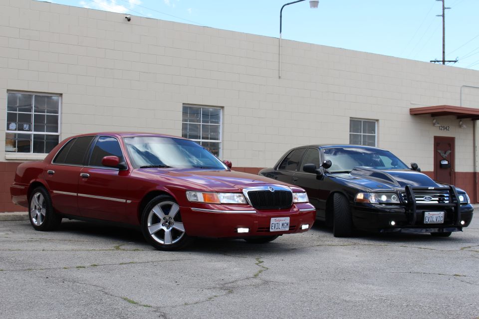 Maroon Mercury Grand Marquis and black Ford sedan parked at angle by tan building