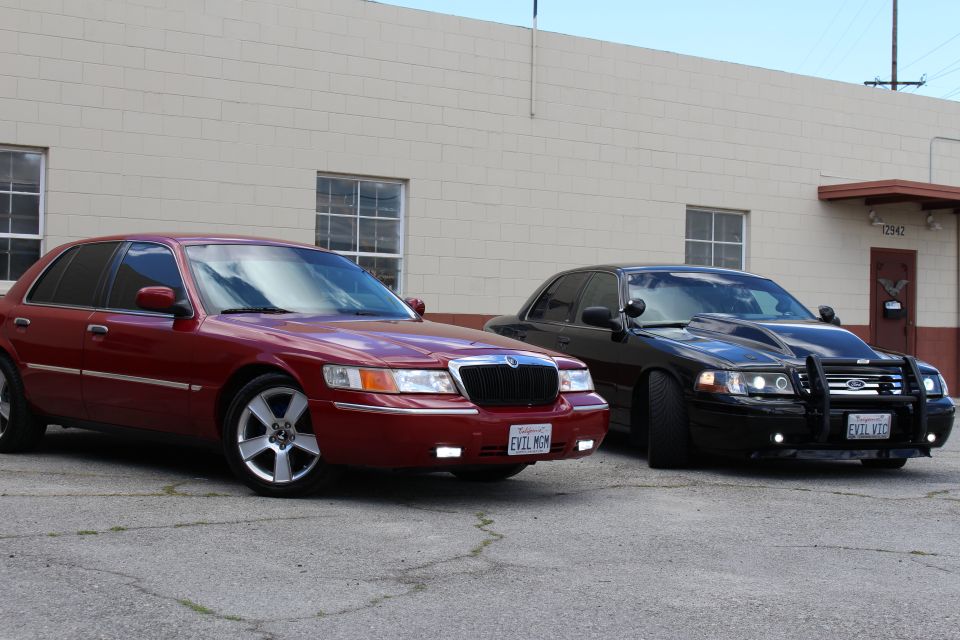 Maroon Mercury sedan and black Crown Victoria with grille guard, three-quarter view