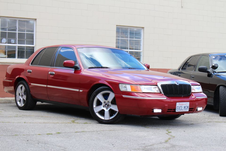 Maroon Mercury Grand Marquis front three-quarter, chrome wheels, by tan building