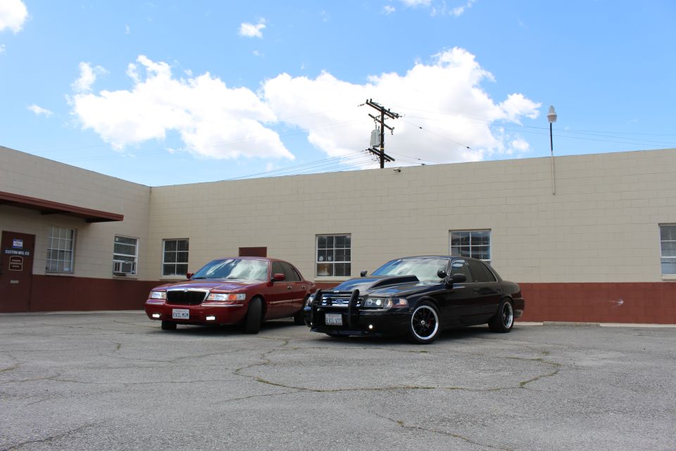 Maroon Mercury and black Crown Victoria parked side by side, wide shot, blue sky