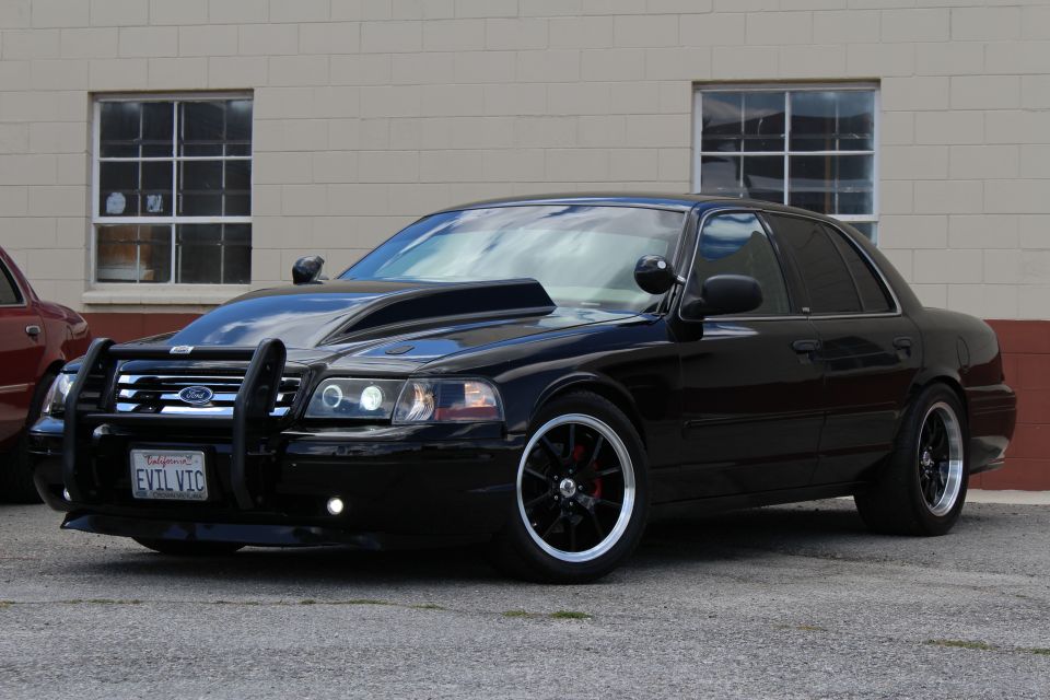 Black Ford Crown Victoria with push bar and EVIL VIC plate parked by brick wall