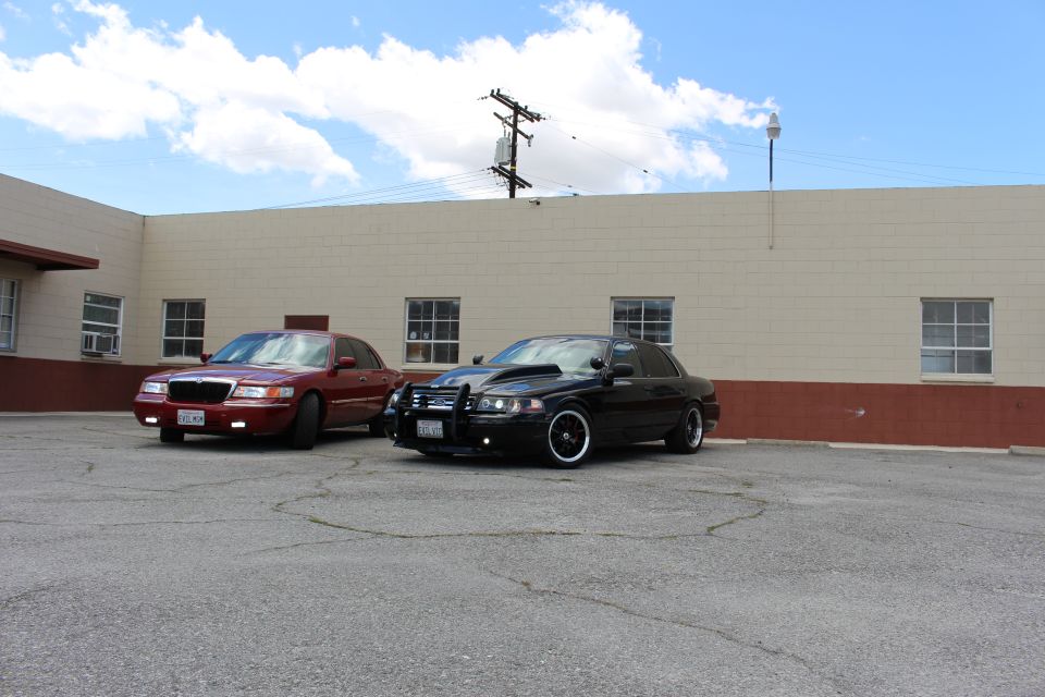 Dark red Mercury sedan and black Crown Victoria parked under power lines and blue sky