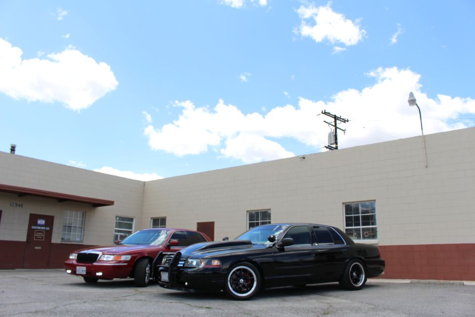 Maroon Mercury sedan and black Crown Victoria parked under tall blue sky