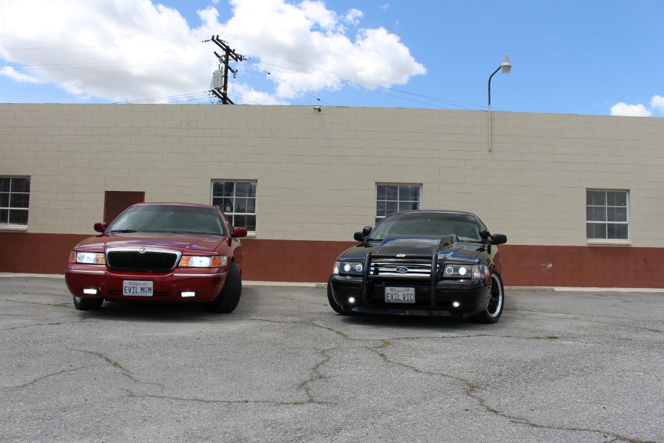 Front view of dark red Mercury and black Ford with push bar parked under blue sky