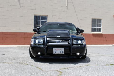 2003 Ford Crown Victoria - blacked-out Ford Crown Victoria with a brush guard, projector headlights and a California 'EVIL VIC' plate, photographed head-on.