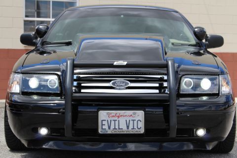 2003 Ford Crown Victoria - black Ford Crown Victoria seen head-on with a brush guard, halo headlights and a California 'EVIL VIC' license plate.