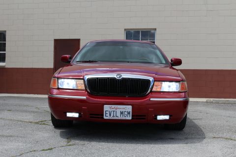 2003 Ford Crown Victoria - dark red Mercury sedan shown from the front, with chrome grille trim and a California 'EVIL MGM' license plate.