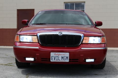2003 Ford Crown Victoria - maroon Mercury sedan photographed straight-on, with a chrome waterfall grille and California 'EVIL MGM' plate.